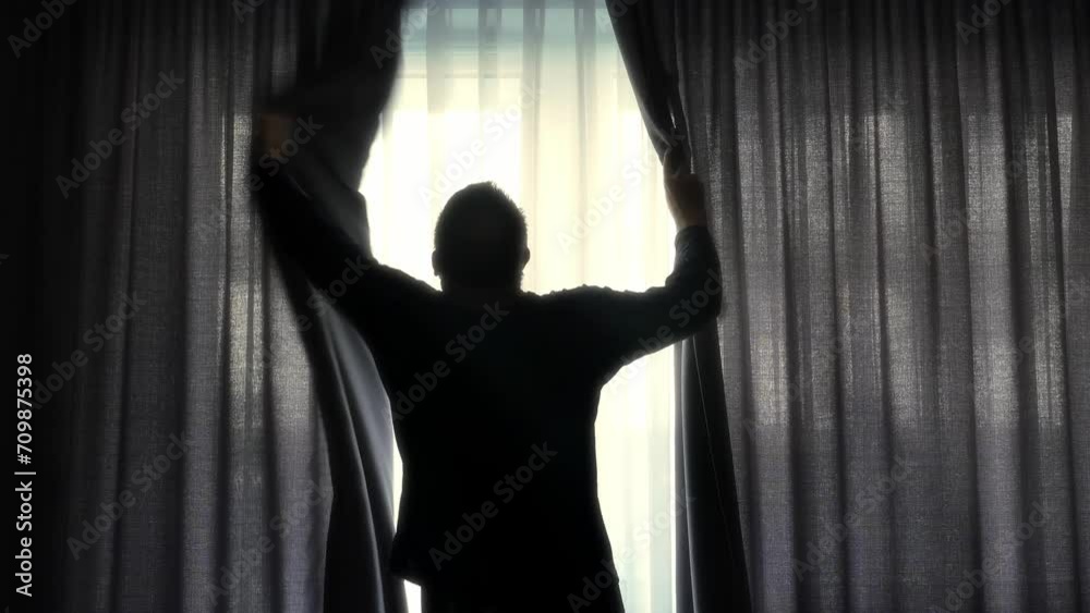 A man drawing back curtains and stretching in front of bedroom window after waking up A man drawing back curtains and stretching in front of bedroom window after waking up