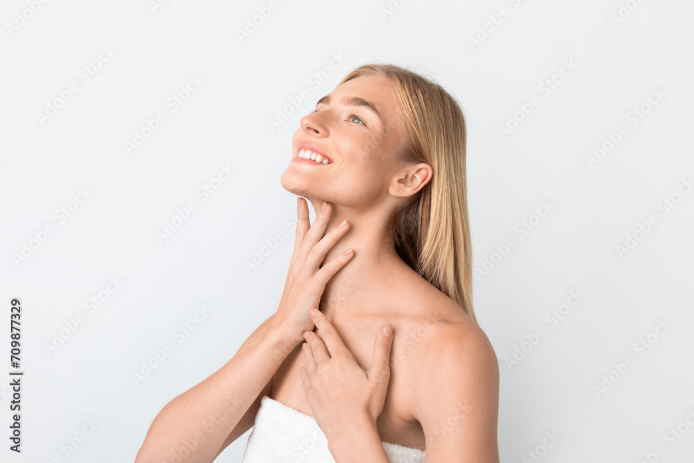 Young blonde woman wrapped in towel delicately touching neck, studio Young blonde woman wrapped in towel delicately touching neck, studio