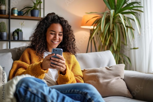 Latin girl sitting on couch using phone in living room at home. Relaxed happy young woman holding mobile cellphone technology doing shopping, communicating online, watching social media, Generative AI
