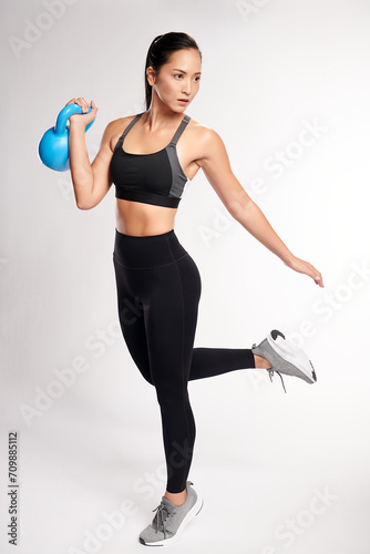 an asian woman is working out with kettlebell wearing the sport exercise suit with white background,
