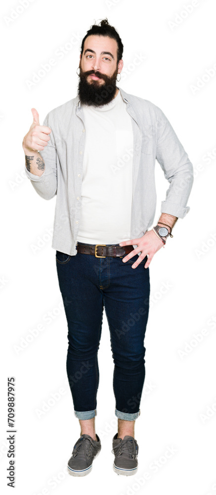 Young man with long hair, beard and earrings doing happy thumbs up gesture with hand. Approving expression looking at the camera showing success. Young man with long hair, beard and earrings doing happy thumbs up gesture with hand. Approving expression looking at the camera showing success.