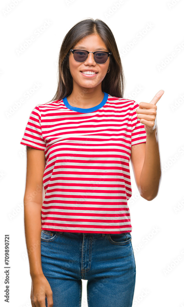 Young asian woman wearing sunglasses over isolated background doing happy thumbs up gesture with hand. Approving expression looking at the camera with showing success. Young asian woman wearing sunglasses over isolated background doing happy thumbs up gesture with hand. Approving expression looking at the camera with showing success.