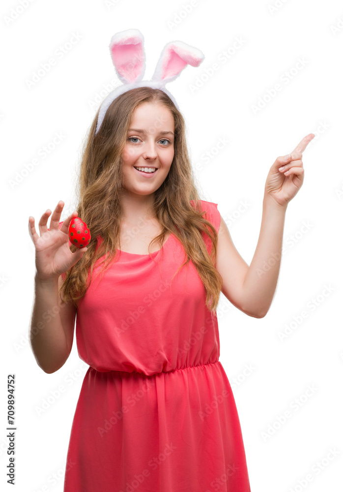 Young blonde woman wearing easter bunny ears very happy pointing with hand and finger to the side Young blonde woman wearing easter bunny ears very happy pointing with hand and finger to the side