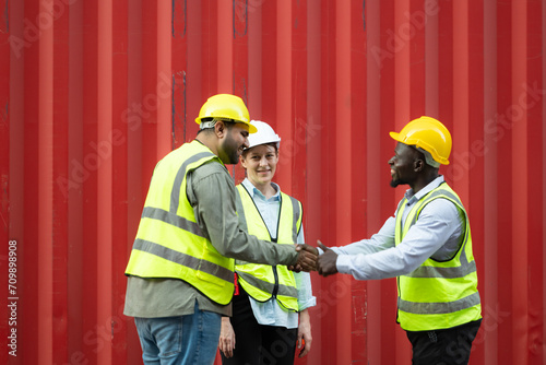Group of workers in a container storage yard greeting each other during breaks in front of container warehouse,