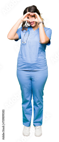 Young adult doctor woman wearing medical uniform Doing heart shape with hand and fingers smiling looking through sign