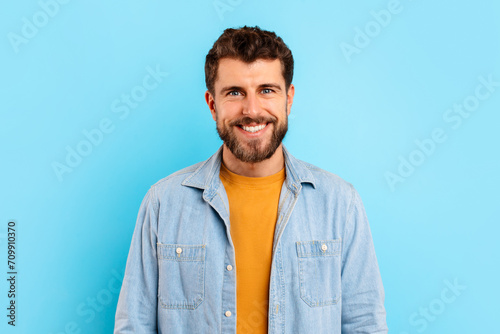Cheerful young bearded man standing against blue studio background © Prostock-studio