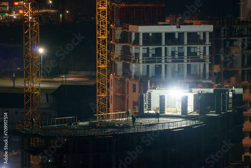 Construction site at night. Cranes working at night over an unfinished house in the light of lanterns. The concept of buying a home on credit  mortgage housing.