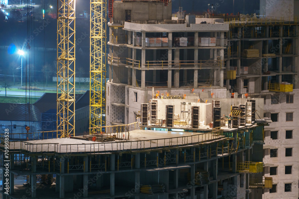 Construction site at night. Cranes working at night over an unfinished house in the light of lanterns. The concept of buying a home on credit, mortgage housing.