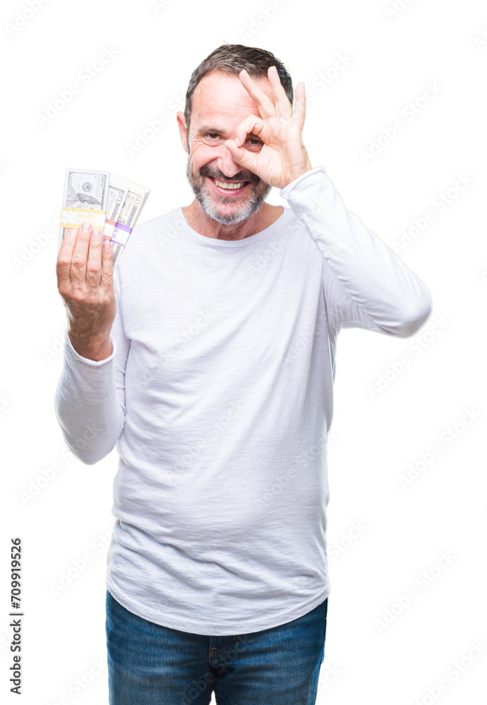 Senior hoary man holding buch of dollars over isolated background with happy face smiling doing ok sign with hand on eye looking through fingers Senior hoary man holding buch of dollars over isolated background with happy face smiling doing ok sign with hand on eye looking through fingers