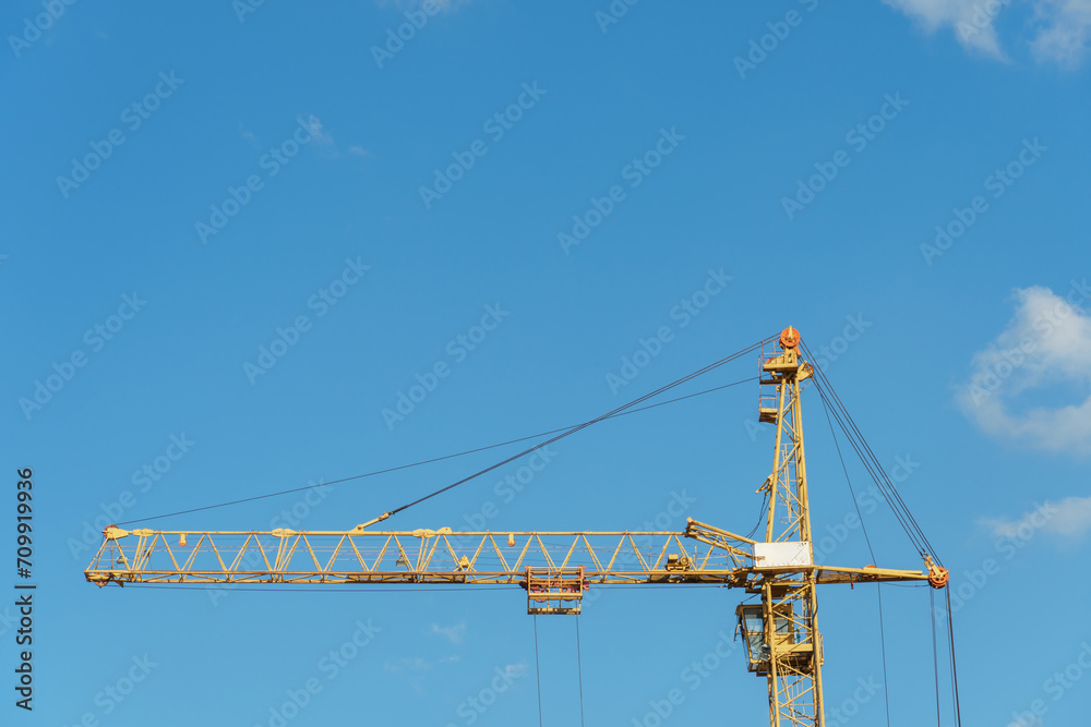 An arrow of working construction cranes against a background of blue sky and clouds. Working machinery on the construction site.