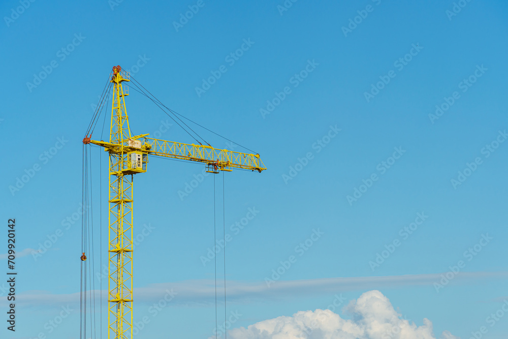 An arrow of working construction cranes against a background of blue sky and clouds. Working machinery on the construction site. An arrow of working construction cranes against a background of blue sky and clouds. Working machinery on the construction site.