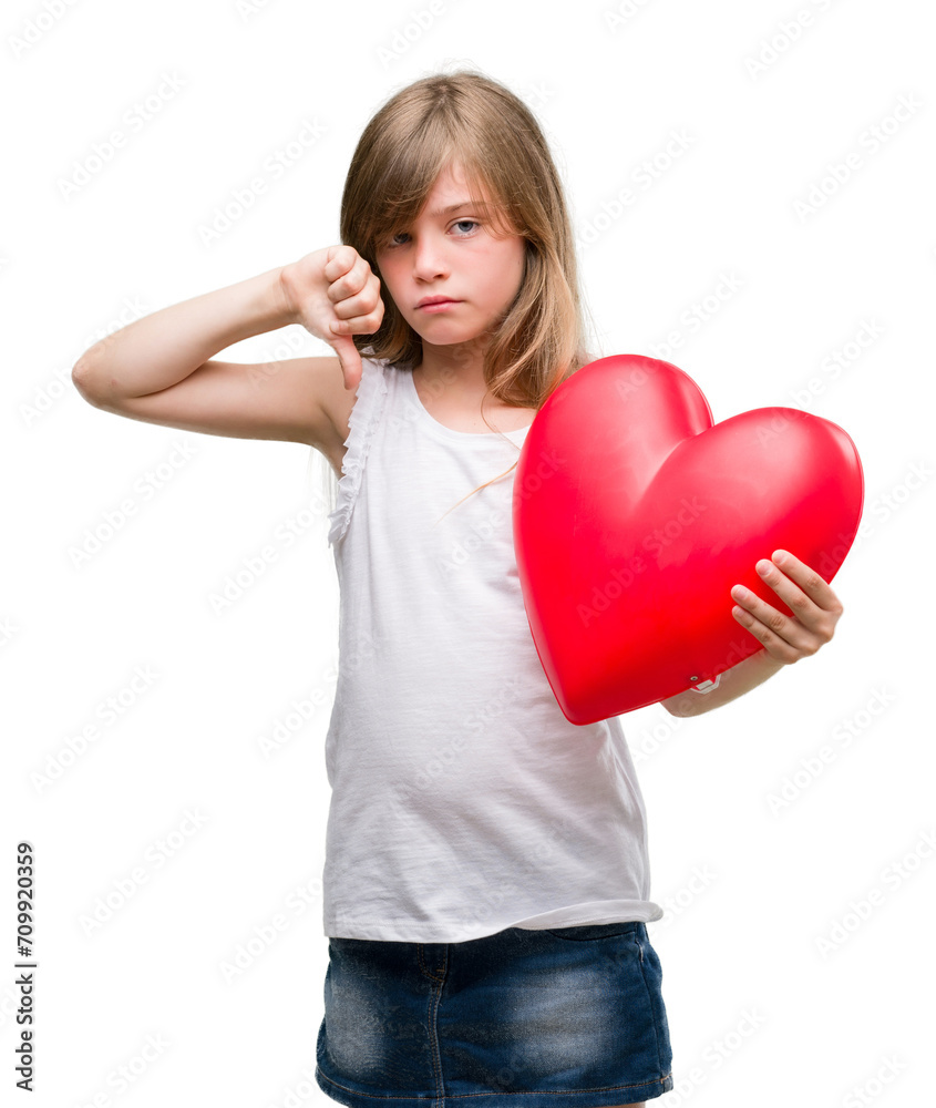 Young blonde toddler holding a red heart with angry face, negative sign showing dislike with thumbs down, rejection concept Young blonde toddler holding a red heart with angry face, negative sign showing dislike with thumbs down, rejection concept