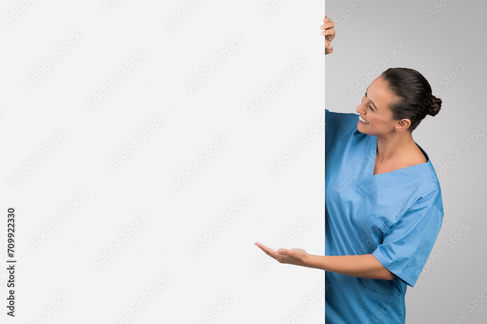 Medical ad. Young european woman physician demonstrating empty space on white placard, showing place for your design Medical ad. Young european woman physician demonstrating empty space on white placard, showing place for your design
