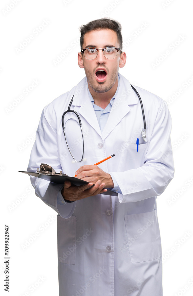 Handsome young doctor man holding a clipboard scared in shock with a surprise face, afraid and excited with fear expression Handsome young doctor man holding a clipboard scared in shock with a surprise face, afraid and excited with fear expression