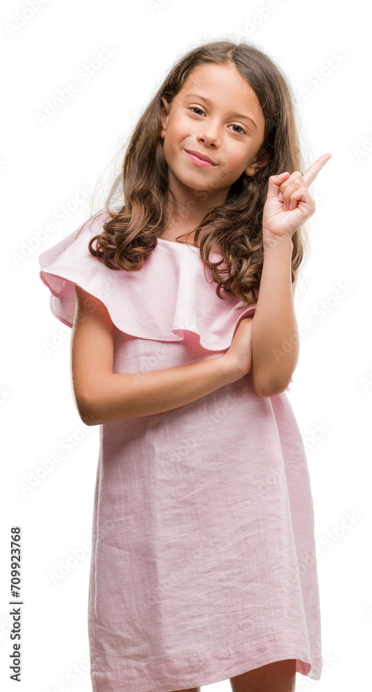 Brunette hispanic girl wearing pink dress with a big smile on face, pointing with hand and finger to the side looking at the camera. Brunette hispanic girl wearing pink dress with a big smile on face, pointing with hand and finger to the side looking at the camera.