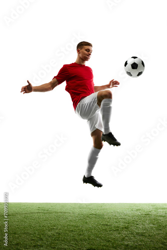 Goal bound Elevation. Professional footballer kicks ball into air, aiming for opponent's gates against background of pure white and lush green grass. Concept of sport games, energy, match, movement. © Lustre