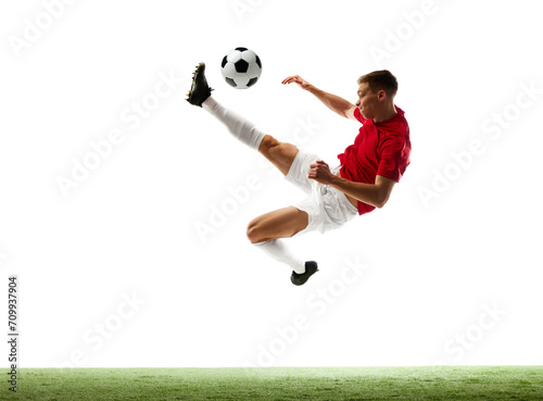 Precision meets flight. Dynamic portrait of a professional football player executing flawless mid-air pass against white background with green grass. Concept of sport games, energy, world cup season.
