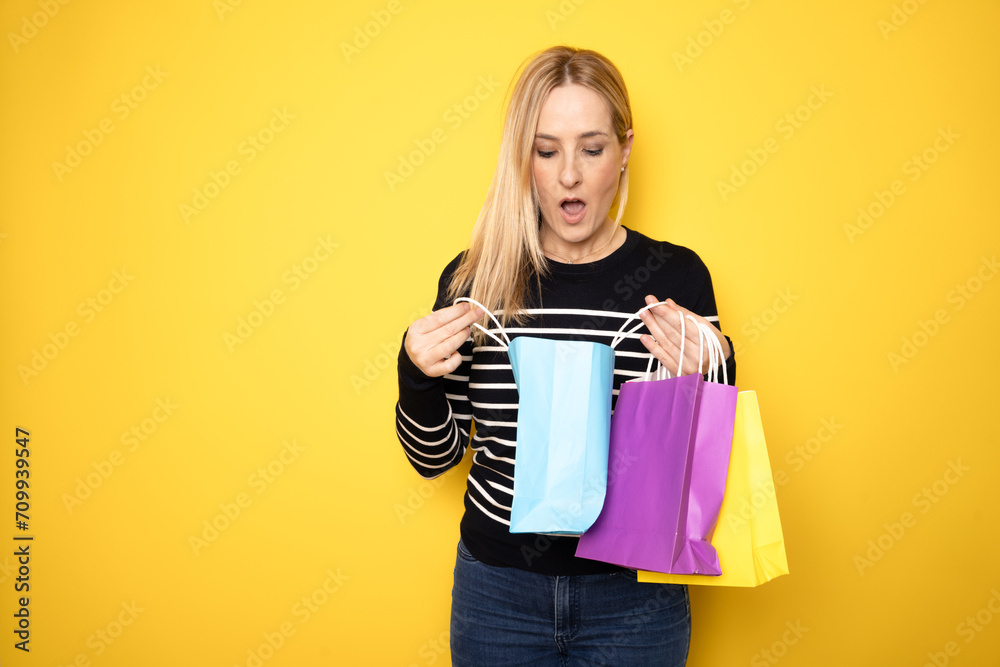 Happy beautiful woman holding red shopping bags looking away isolated on yellow background, copy space. Shopping, sale, black Friday Happy beautiful woman holding red shopping bags looking away isolated on yellow background, copy space. Shopping, sale, black Friday