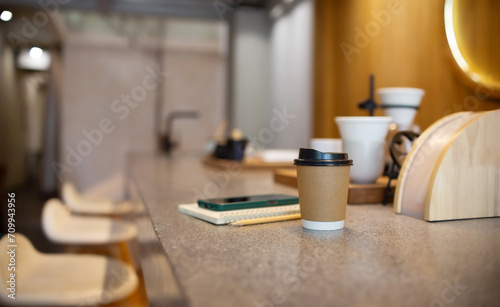 Coffee cup with mobile placed on notebook on mable counter with coffee equipment for coffee drip on counter bar, people use mobile technology easy work in cafe