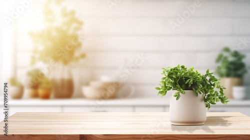 Spacious wooden table for product display or sample in unfocused white kitchen with chopping block and foliage in Nordic design during sunrise.