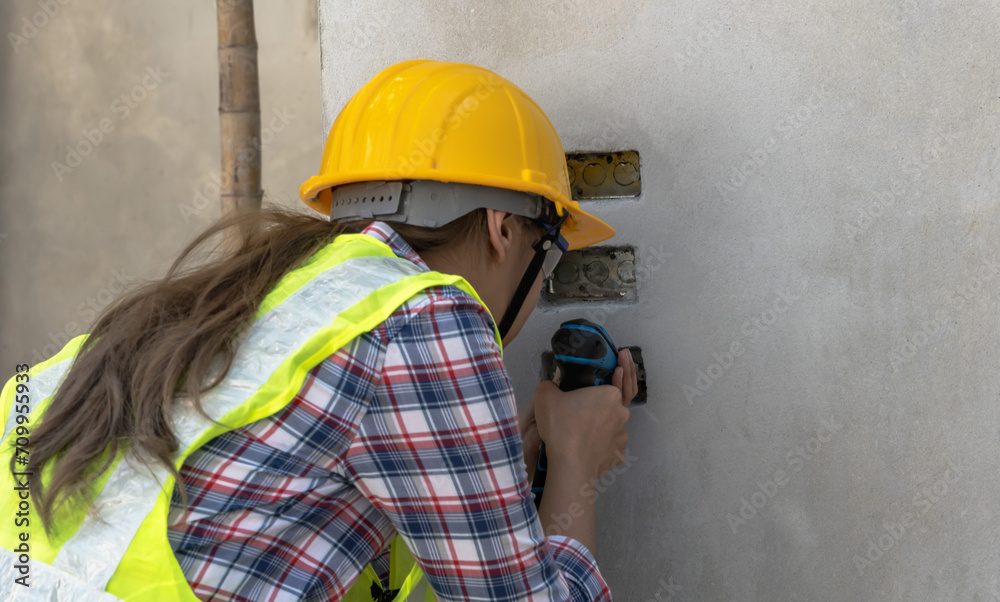 Female electrician woman drilling electric outlet on wall in construction site Female electrician woman drilling electric outlet on wall in construction site