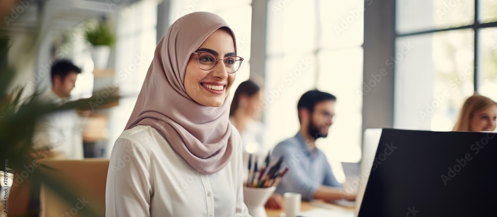 Diverse young colleagues working together in a modern office. Muslim woman smiling after completing a task. Diverse young colleagues working together in a modern office. Muslim woman smiling after completing a task.