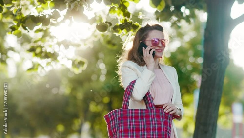 happy stylish woman in pink dress and white jacket in the city talking on a smartphone. photo