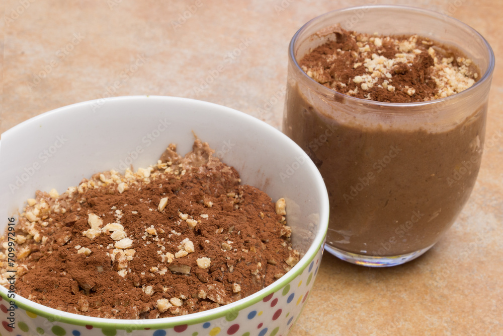 A close-up of a glass and a bowl filled with a chocolate mousse enriched with cocoa and almonds on a countertop. Quick and easy Desserts. A close-up of a glass and a bowl filled with a chocolate mousse enriched with cocoa and almonds on a countertop. Quick and easy Desserts.