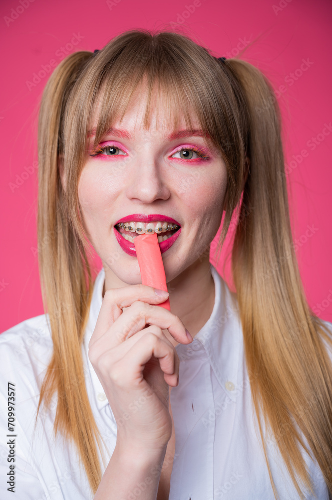 Portrait of a young woman with braces and bright makeup chewing gum on a pink background. Vertical photo. Portrait of a young woman with braces and bright makeup chewing gum on a pink background. Vertical photo.