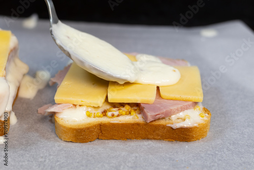 Preparing process of Croque monsieur and croque madame, grilled sandwiches with sliced ham, melted cheese, dijon mustard and poached egg on  bechamel sauce.