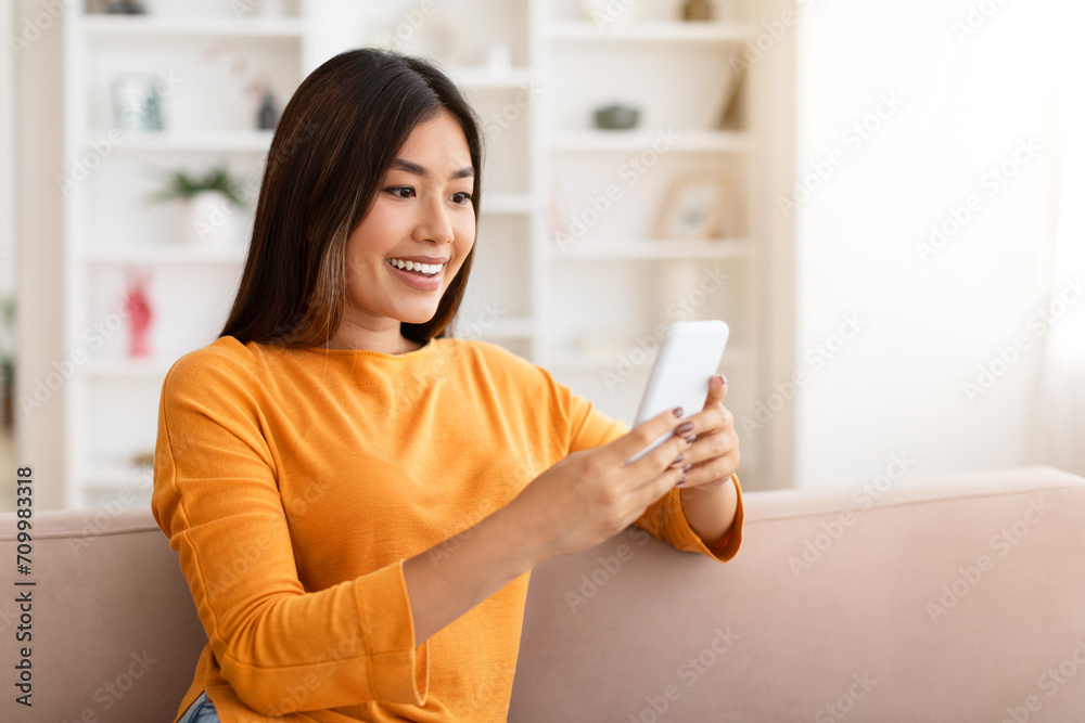 Happy millennial chinese woman relaxing on couch with phone Happy millennial chinese woman relaxing on couch with phone