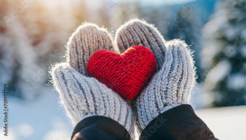 female hands in knitted mittens with knitted heart on a snowy winter day