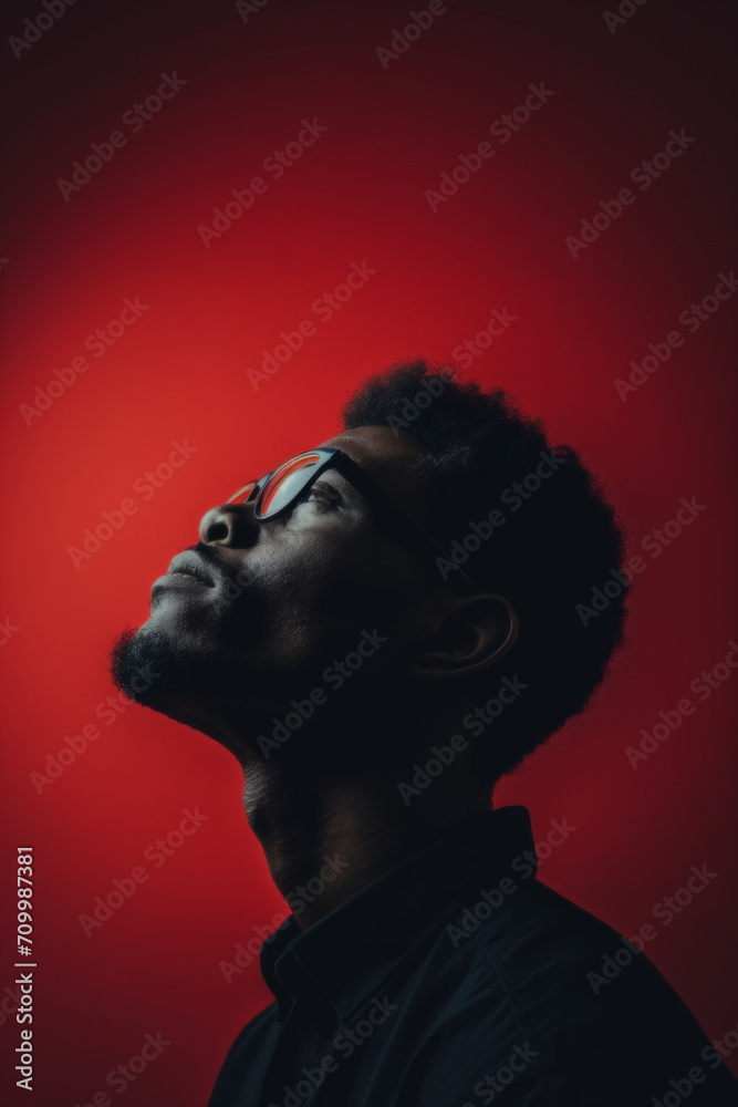Profile side view portrait of a young African American man wearing glasses looking up against red background. Black History Month Concept. For banner, card, poster Profile side view portrait of a young African American man wearing glasses looking up against red background. Black History Month Concept. For banner, card, poster