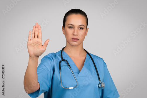 Serious european female doctor in blue uniform showing stop gesture, refusing something, saying no to viruses photo