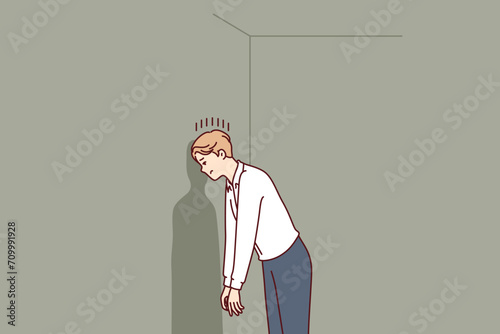 Depressed man in hopeless situation is banging head against wall trying to come up with original solution to problem. Guy victim of hopeless situation needs psychological support or advice