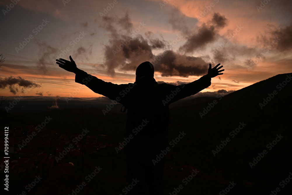 Silhouette of a man on top of a mountain with a sunset in the background.
