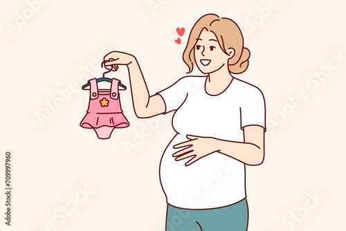 Pregnant woman with clothes for little girl in hand, dreaming birth of daughter. Pregnant lady, mother unborn child, chooses dress, imagining happy motherhood and opportunity to spend time with child