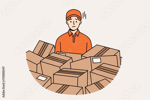 Sad man courier stands among scattered cardboard boxes, suffering from overload associated with logistics problems. Courier guy from delivery service or postal company needs help delivering parcels.