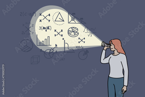 Woman looks at mathematical formulas on wall using flashlight preparing to enter college or university. Girl sees mysterious mathematical drawings studying algebra or economic audit. photo