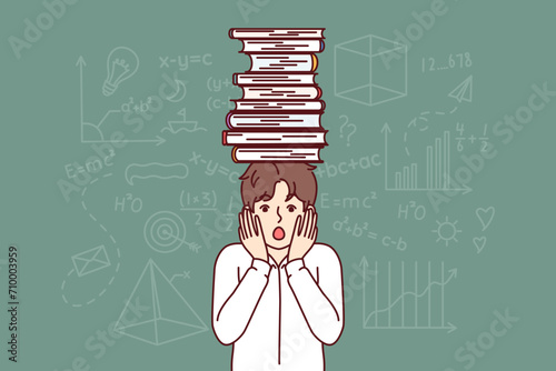 Frightened schoolboy with books on head feels fear of exam, stands near blackboard with formulas. Schoolboy experiences stress due to complex educational program for primary school students.
