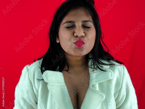 Fotografi Portrait of a woman puckering lips for a kiss against a red background