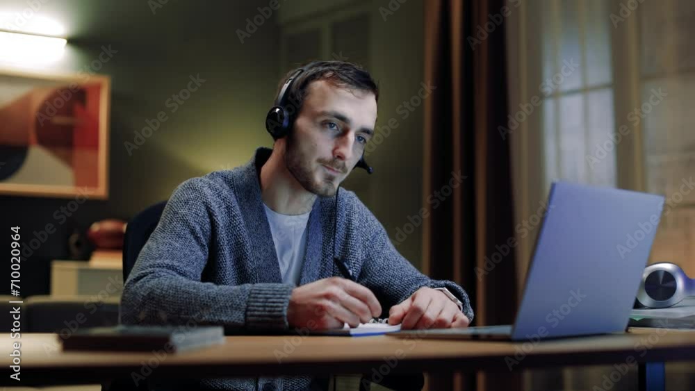 Man conducting online lesson at home. Male working distantly. Man holding pen and making notes. Male wearing headphones and looking at laptop. Man working from home. Diversity of professions. Man conducting online lesson at home. Male working distantly. Man holding pen and making notes. Male wearing headphones and looking at laptop. Man working from home. Diversity of professions.