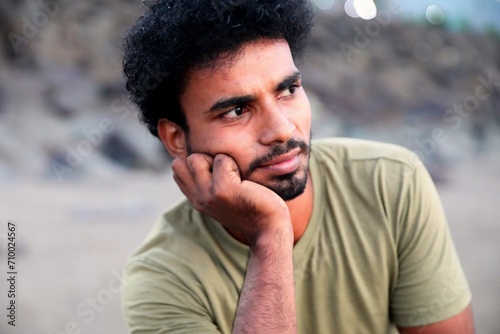Thoughtful young man with a beard resting his chin on his hand looking away with a blurred background