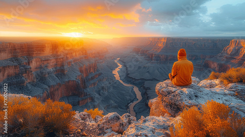 A solitary figure sits at the precipice of a breathtaking canyon, the warm hues of the setting sun casting a golden glow on the rugged terrain below, creating a moment of introspec photo