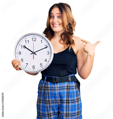 Young beautiful caucasian woman holding big clock pointing finger to one self smiling happy and proud