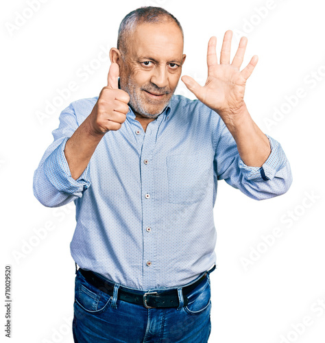 Senior man with grey hair and beard wearing casual blue shirt showing and pointing up with fingers number six while smiling confident and happy.