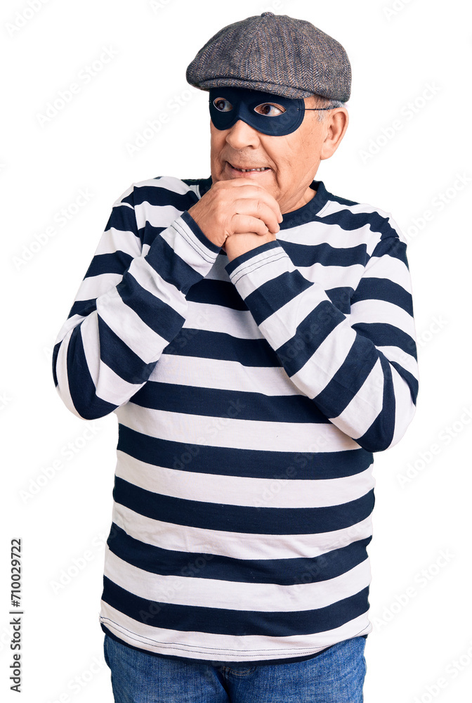 Senior handsome man wearing burglar mask and t-shirt laughing nervous and excited with hands on chin looking to the side Senior handsome man wearing burglar mask and t-shirt laughing nervous and excited with hands on chin looking to the side