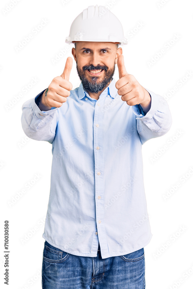Young handsome man wearing architect hardhat approving doing positive gesture with hand, thumbs up smiling and happy for success. winner gesture. Young handsome man wearing architect hardhat approving doing positive gesture with hand, thumbs up smiling and happy for success. winner gesture.