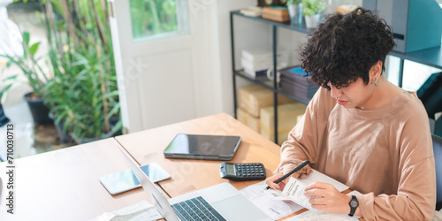 A Young Asian businesswoman is checking financial documents, calculating bills or taxes expense or payment at home, using laptop and calculator, investment or insurance planning, money saving control.