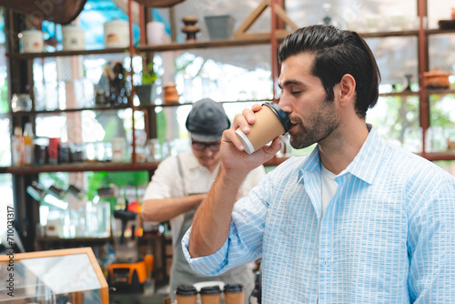 Smart Caucasian male enjoy drinking a takeaway hot coffee in front of coffee shop or café bar or counter, Refreshment, happiness good taste and aroma from coffee. Man is holding hot americano or latte